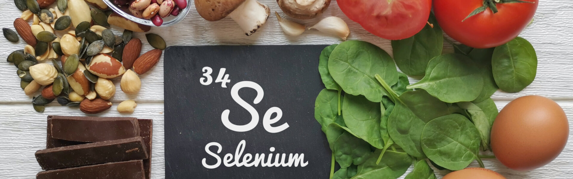 Board labeled "34 Se Selenium" surrounded by nuts, seeds, mushrooms, tomatoes, garlic, spinach, and eggs on a white wooden surface.