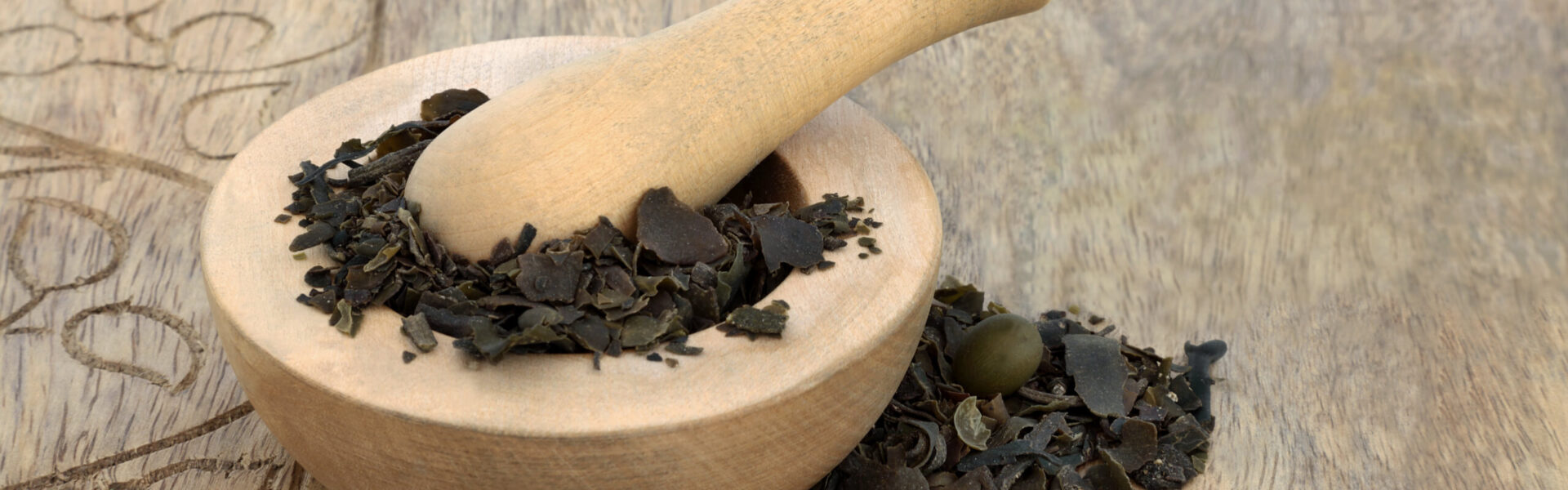 Assorted magnesium-rich foods rest on a wooden surface: bananas, avocado, almonds, chickpeas, cacao, cabbage, parsley, and seeds. A sign reads "Mg Magnesium" amidst the arrangement.