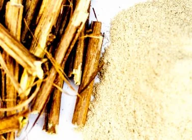 Bundled wooden sticks lie next to a small pile of beige powder on a smooth, white surface.